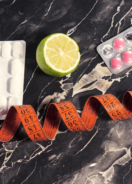 Collage aus einer halben Limette, einem geringelten Maßband und einer Packung Tabletten auf einer Marmorplatte