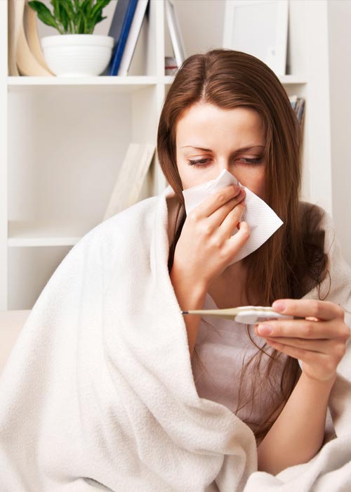 Eine junge Frau , die sich mit der einen Hand die Nase putzt und mit der anderen Hand ein Fieberthermometer hält